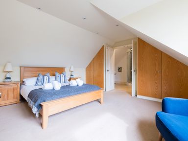 A bedroom with a wooden bed and bedside tables a blue chair and built in wooden wardrobes at Silverdale in Rock