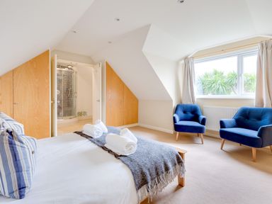 A bedroom with a bed and folded towels a shower and two blue chairs by a window at Silverdale in Rock