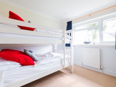 A bedroom with white bunk beds red and blue pillows and a window with blue curtains at Silverdale in Rock