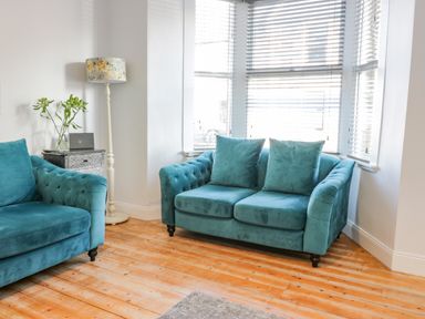 A living room with two teal sofas a floor lamp and a side table with flowers at The Lazy Seal in Spittal