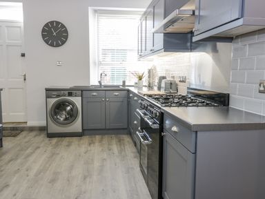 A kitchen with gray cabinets a washing machine a gas stove and a clock on the wall at The Lazy Seal in Spittal