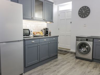 A kitchen with grey cabinets a fridge microwave washing machine and a clock on the wall at The Lazy Seal in Spittal
