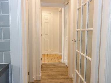 A hallway with wooden flooring and white doors including a door with glass panels at The Lazy Seal in Spittal