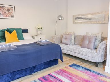 A bedroom with a bed with colorful pillows a sofa and a floor lamp at The Lazy Seal in Spittal