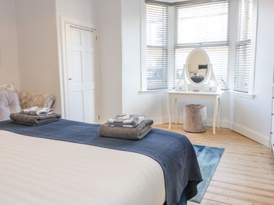 A bedroom with a bed with folded towels a vanity table with mirror and a stool by windows at The Lazy Seal in Spittal