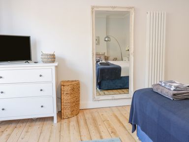 A bedroom with a white dresser and TV a large mirror and a bed with towels at The Lazy Seal in Spittal
