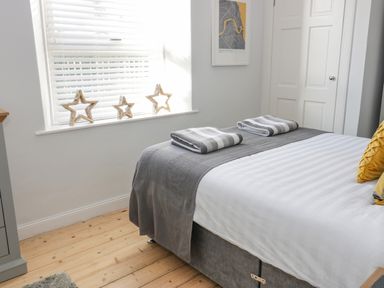 A bedroom with a bed covered in white and gray linens two folded towels on the bed wooden stars on the windowsill and a framed map on the wall at The Lazy Seal in Spittal