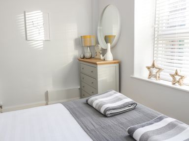 A bedroom with a bed covered with a gray blanket and folded towels next to a dresser with a lamp and mirror at The Lazy Seal in Spittal
