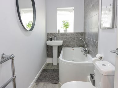 A bathroom with a bathtub, sink, toilet, round mirror, and window with a plant at The Lazy Seal in Spittal