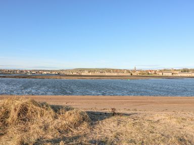 A beach with grass and water with houses and buildings in the background at The Lazy Seal in Spittal