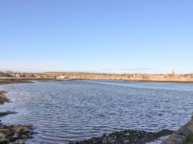 A wide river with a bridge and buildings along the shore under a clear sky at The Lazy Seal in Spittal
