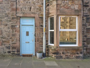 A blue door and a window on a stone building with a potted plant and a street lamp at The Lazy Seal in Spittal