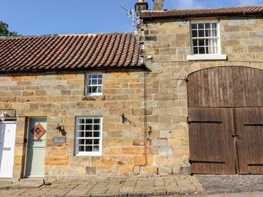 Stone building with tiled roof green door windows and large wooden barn door at Michaelmass Cottage in Castleton