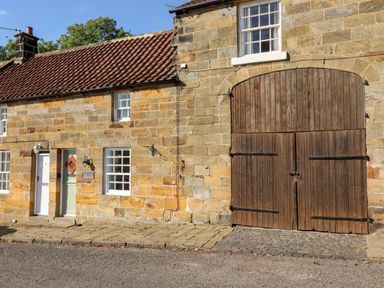 Exterior of a stone building with tiled roof two doors and large wooden barn door at Michaelmass Cottage in Castleton