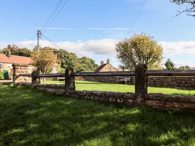 A grassy area with a wooden fence and stone wall near houses and trees at Michaelmass Cottage in Castleton