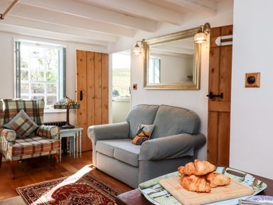 A living room with a plaid armchair a blue loveseat a wooden door and croissants on a table at Michaelmass Cottage in Castleton