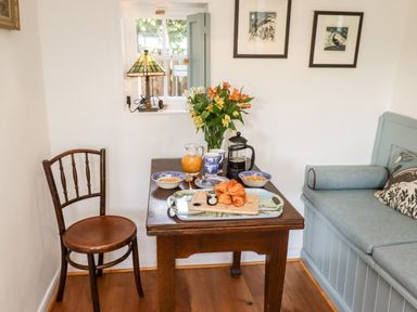 A dining area with a wooden table set with croissants and bowls a wooden chair and a cushioned bench at Michaelmass Cottage in Castleton