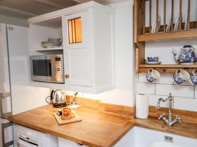 A kitchen countertop with a microwave kettle croissants and a wooden dish rack with blue and white teapot cups and plates at Michaelmass Cottage in Castleton