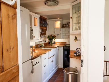 A small kitchen with white cabinets wooden countertops a refrigerator a dishwasher a sink flowers on the counter and a stove at Michaelmass Cottage in Castleton