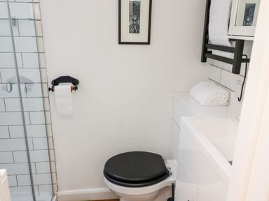 A bathroom with toilet with black seat cover shower with glass door and towels on counter at Michaelmass Cottage in Castleton