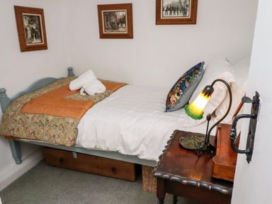 A small bedroom with a single bed a wooden side table and framed pictures on the wall at Michaelmass Cottage in Castleton