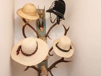 A collection of hats including a pith helmet, a police helmet, and two straw hats hanging on antlers mounted on a wall at Michaelmass Cottage in Castleton