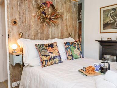 A bedroom with a bed with patterned pillows a wooden wreath on the wall and breakfast on the bed at Michaelmass Cottage in Castleton