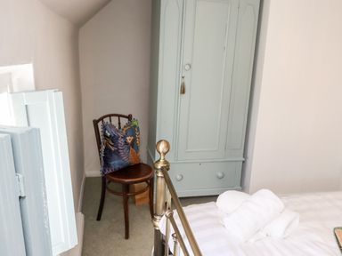A bedroom corner with a wooden chair with a cushion next to a pale blue wardrobe and a bed with white towels at Michaelmass Cottage in Castleton