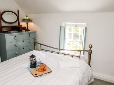A bedroom with a brass bed frame a blue dresser with a mirror and a stained glass lamp at Michaelmass Cottage in Castleton