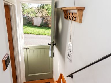 An open split door leading outside with a wooden coat rack and hanging decoration inside at Michaelmass Cottage in Castleton