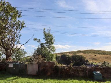 A garden area with stone walls trees grassy hill and power lines at Michaelmass Cottage in Castleton