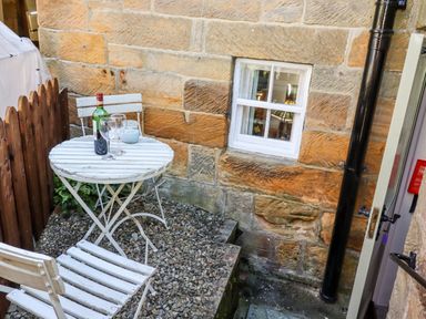 A small outdoor seating area with a white table and chairs a bottle of wine and two glasses on the table at Michaelmass Cottage in Castleton