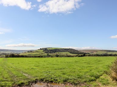 A green grassy field with hills and trees in the background under a blue sky at Michaelmass Cottage in Castleton
