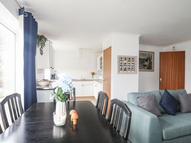 A dining area with a black table and chairs next to a kitchen with white cabinets and a blue sofa with cushions at 5 Ger Y Nant in Llanbedrog