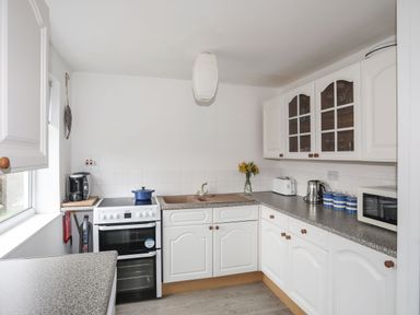 A kitchen with white cabinets a stove a sink and countertop appliances at 5 Ger Y Nant in Llanbedrog