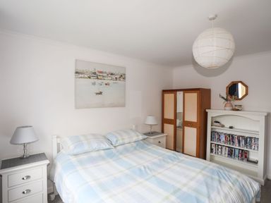 A bedroom with a bed two bedside tables with lamps a wardrobe and a bookshelf filled with DVDs at 5 Ger Y Nant in Llanbedrog