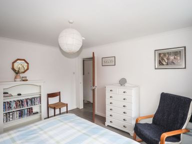 A bedroom with a bed a chair a white chest of drawers a bookshelf and framed pictures on the walls at 5 Ger Y Nant in Llanbedrog
