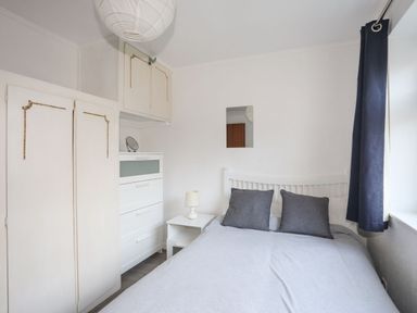 A bedroom with a bed bedside table lamp chest of drawers and window with dark curtains at 5 Ger Y Nant in Llanbedrog