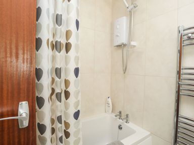 A bathroom with a bathtub shower and a heart patterned shower curtain at 5 Ger Y Nant in Llanbedrog