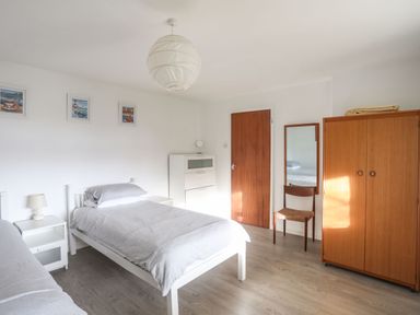 A bedroom with two beds a white dresser a wooden wardrobe a chair with a mirror and a wooden door at 5 Ger Y Nant in Llanbedrog