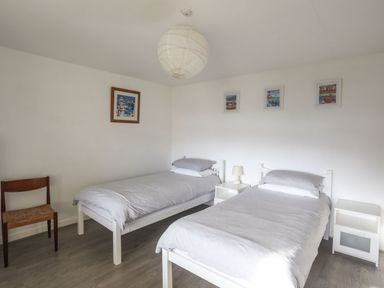 A bedroom with two single beds bedside tables a wooden chair and framed pictures on the walls at 5 Ger Y Nant in Llanbedrog