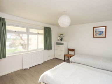 A bedroom with two single beds a white chest of drawers a wooden chair green curtains and a framed picture on the wall at 5 Ger Y Nant in Llanbedrog