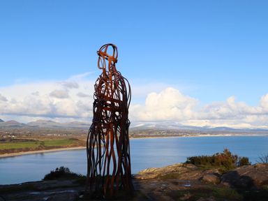 An outdoor metal sculpture of a human figure overlooking a body of water with mountains and clouds in the background at 5 Ger Y Nant in Llanbedrog