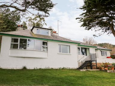 The exterior of a white house with multiple windows a small set of black metal stairs and a grassy lawn at Rocklea Seaside Cottage in Newcastle County Down
