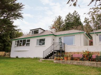 A white single-story house with a small staircase leading to a sliding glass door and potted plants on a raised platform in a garden at Rocklea Seaside Cottage in Newcastle County Down