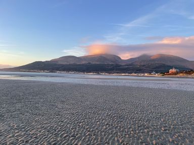 A beach with rippled sand and water in front of mountains with clouds and buildings at Rocklea Seaside Cottage in Newcastle County Down
