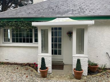 Front entrance of a white house with two potted plants and a small porch at Rocklea Seaside Cottage in Newcastle County Down