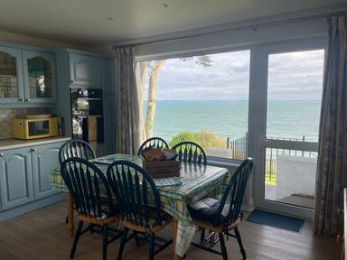 A kitchen with blue cabinets a dining table with six chairs and a large window overlooking the sea at Rocklea Seaside Cottage in Newcastle County Down
