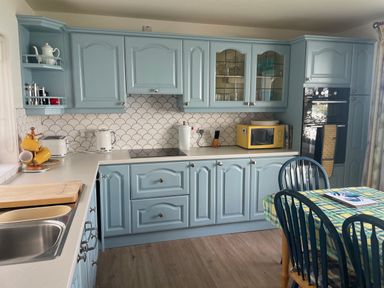 A kitchen with blue cabinets a yellow microwave a dining table with chairs and a checked tablecloth at Rocklea Seaside Cottage in Newcastle County Down
