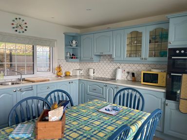 A kitchen with blue cabinets a table with a checkered tablecloth and blue chairs at Rocklea Seaside Cottage in Newcastle County Down